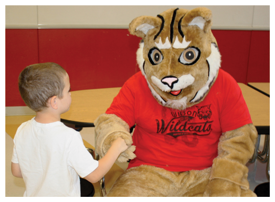 一个年轻的学生正在和一只野猫吉祥物握手
