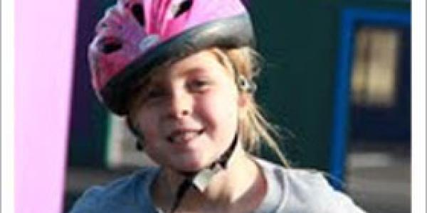 年轻的女孩骑着自行车，戴着粉红色的头盔
