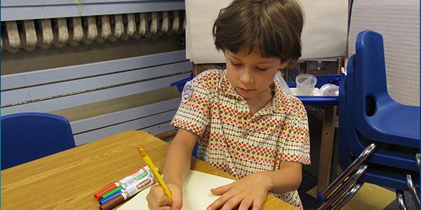 一个小孩子坐在桌子前在一张纸上写字。