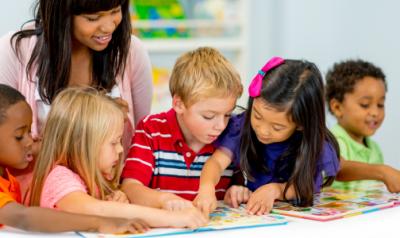五个孩子和他们的老师一起看图画书。