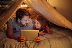 一个成年人读下一个孩子从平板电脑屏幕一个帐篷在室内。